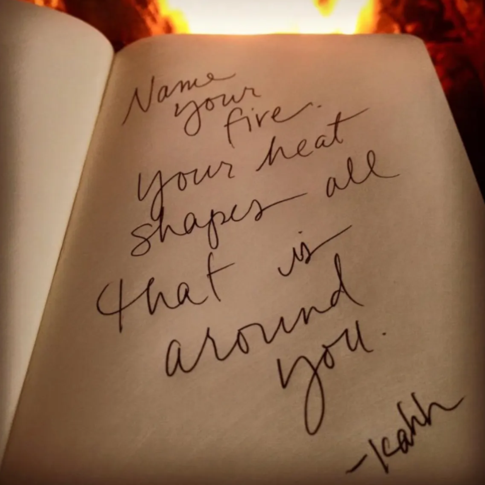 Notebook page with a handwritten quote, set against a warm fire: 'Name your fire, your heart shapes all that is around you.'
